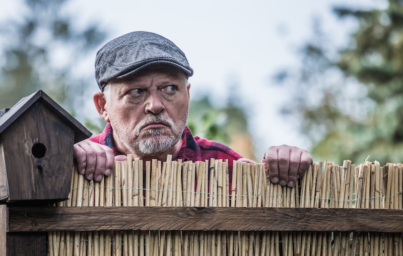 Nachbar schaut über Gartenzaun